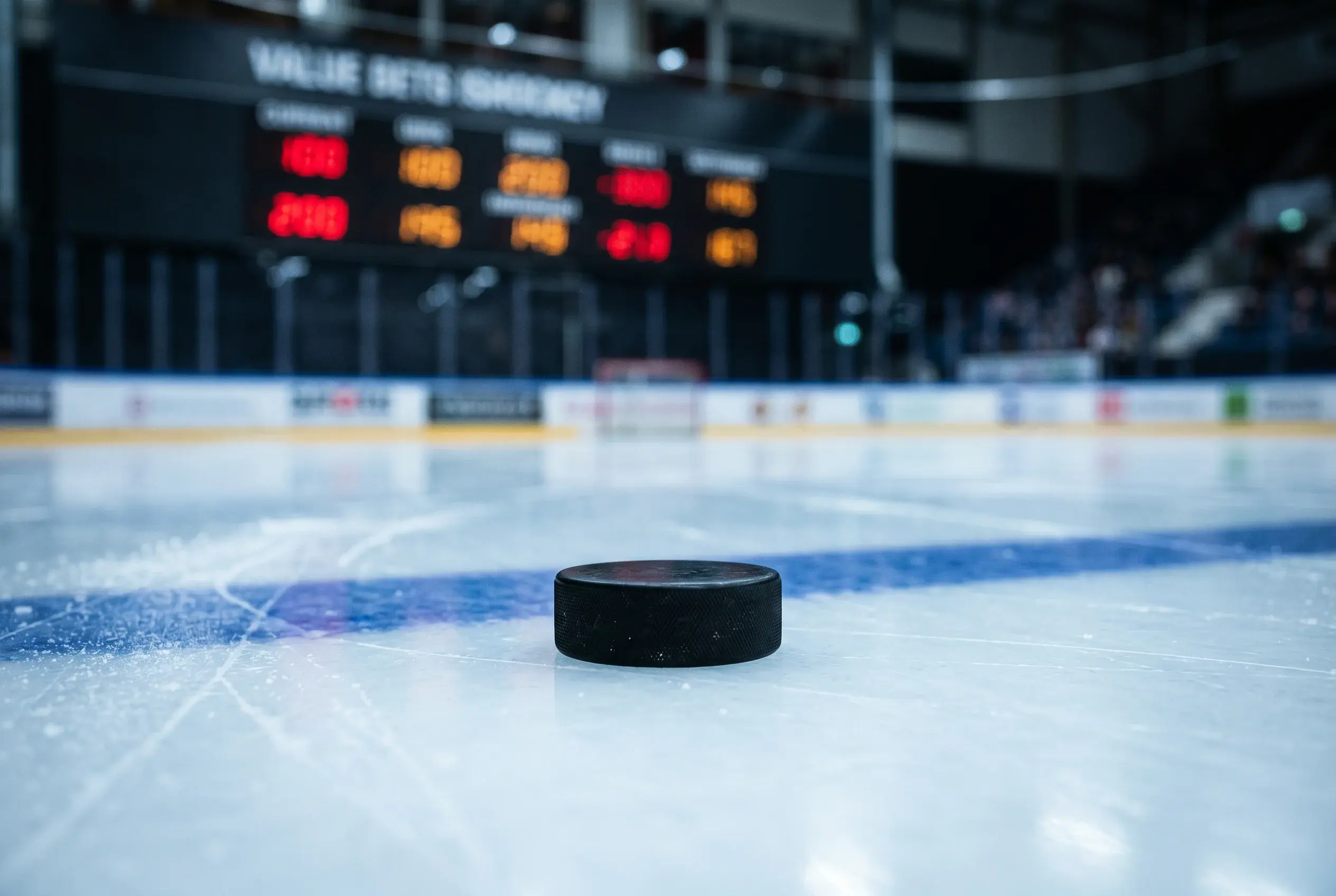 Nærbillede af en ishockeypuck på isen med odds-tavle i baggrunden